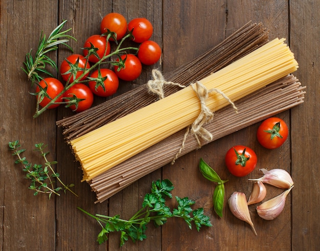 Three types of spaghetti, tomatoes and herbs on wood