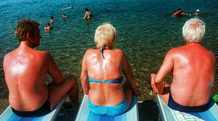 Photo three vacationers sitting on chairs sunbathing and looking on swiming people in sea