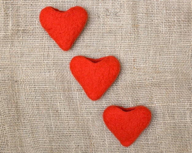 Three valentines made of felted wool in the form of hearts on sacking