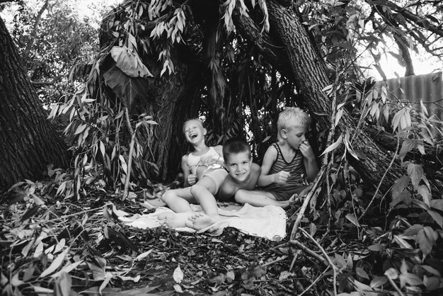 Three village children are playing in a hut which they themselves have built from leaves and twigs Wooden house in the forest Black and white photography