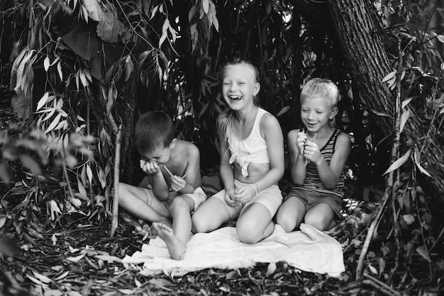 Three village children are playing in a hut which they themselves have built from leaves and twigs Wooden house in the forest Black and white photography