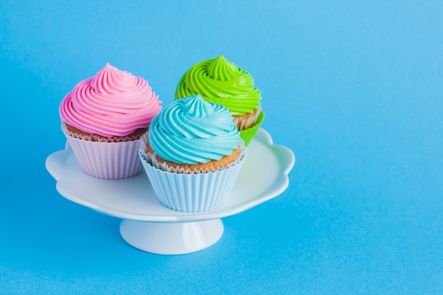 Three vivid colous cupcakes with cream cheese on the blue background