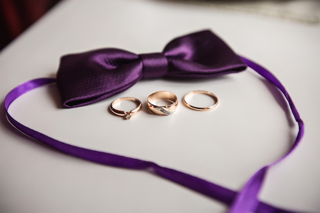 Three wedding rings: one for bride, one for groom and proposal ring near purple bow tie