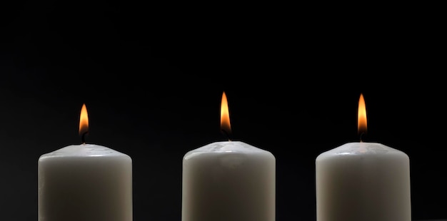 Three white candles with a flame on a black background