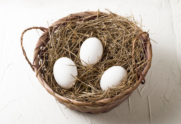 Three white chicken eggs in a hay nest on a white background.