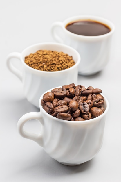 Three white cups with coffee beans, ground coffee and coffee drink. White background. Close up