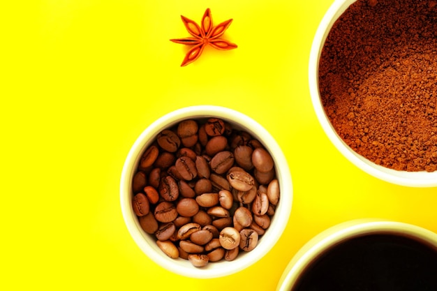 Three white cups with ground coffee beans black brewed coffee in the rays on a yellow background