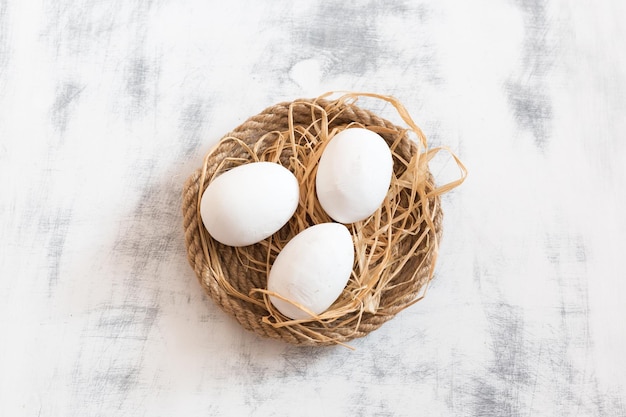 Three white Easter eggs lying on a tray made of twine with some hay