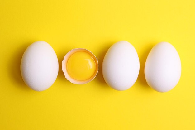 Three white eggs are lined up on a yellow background