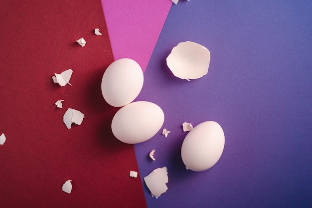 Three white eggs with eggshell pieces on red, pink and blue