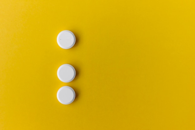 Three white round pills on yellow