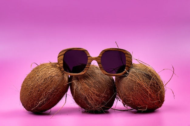 Three whole coconuts and wooden glasses on a pink background