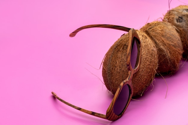 Three whole coconuts and wooden glasses on a pink background