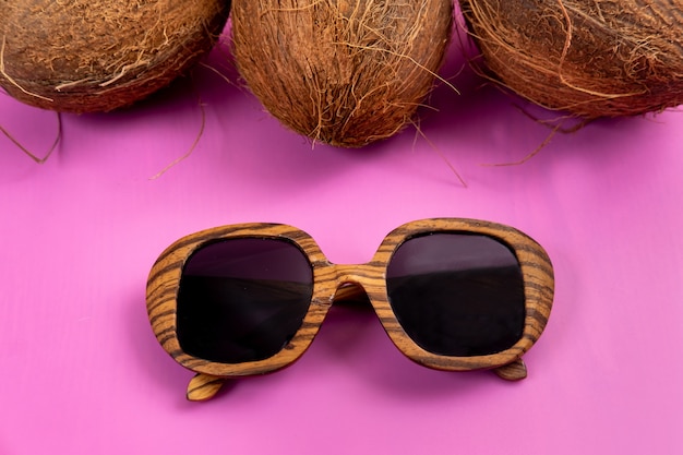 Three whole coconuts and wooden glasses on a pink background