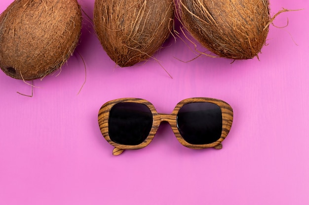 Three whole coconuts and wooden glasses on a pink background.