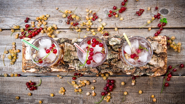 Three wild currant Cocktail with ice on a wooden table.