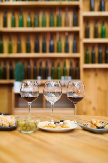 Three wineglasses and snack for sommelier on wooden table inside cellar of luxury restaurant