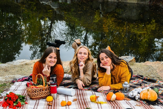 Фото Лучшие подруги трех женщин на осеннем пикнике в парке. красочный плед, термос и пампинки. друзья веселятся на открытом воздухе. теплый осенний октябрьский день