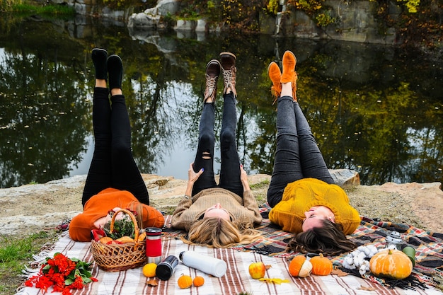 Three women best friends at autumn picnic in the park. Colorful plaid, thermos and pumpins. Friends having fun outdoors. Warm autumn October day