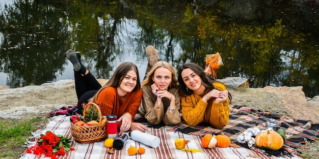 Three women best friends at autumn picnic in the park. Colorful plaid, thermos and pumpins. Friends having fun outdoors. Warm autumn October day