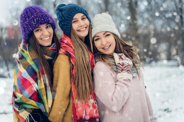 Foto tre amiche donne all'aperto in cappelli a maglia che si divertono in un gruppo di giovani femmine in tempo freddo innevato