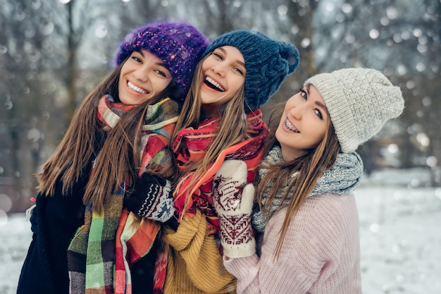 Three women friends outdoors in knitted hats having fun on a snowy cold weather