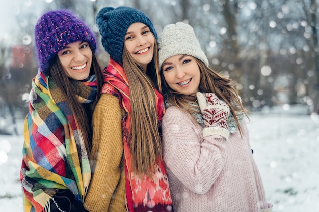 Three women friends outdoors in knitted hats having fun on a snowy cold weather