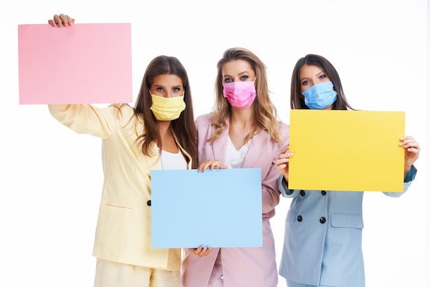 three women in pastel suits holding billboard posing over white background