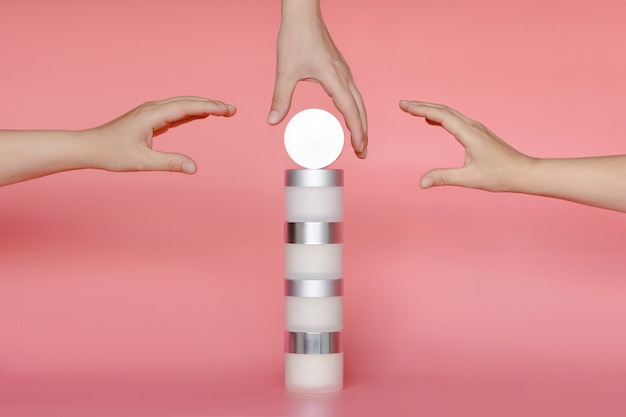 Three women's hands reach for a stack of round cans of cream and serum for face and body. 