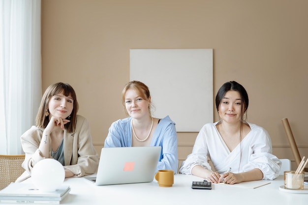 three women sitting at a table with a laptop and a coffee cup