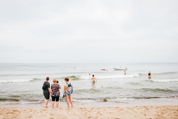 Three women stand on beach and take pictures of him on phone