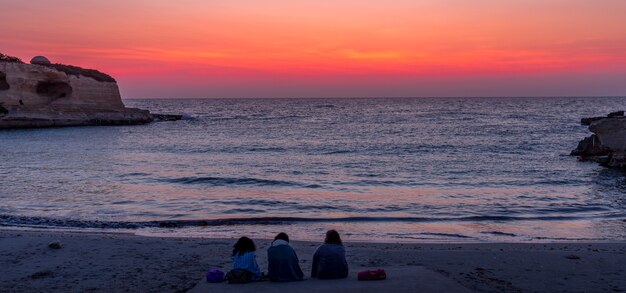 海の前で日の出を待つ3人の女性（南イタリア、プーリア地方）。友情、旅行、冒険の概念。