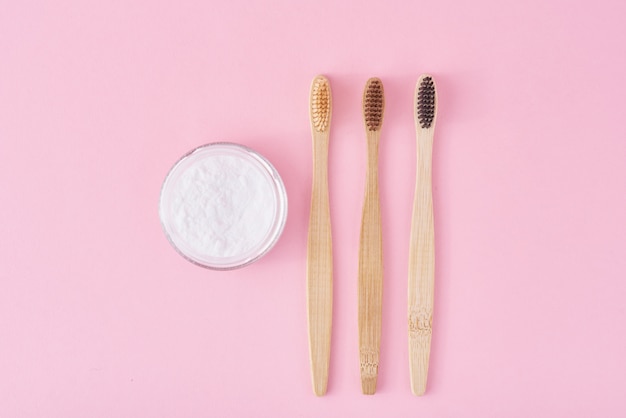 Three wooden bamboo toothbrushes and baking soda powder in glass jar