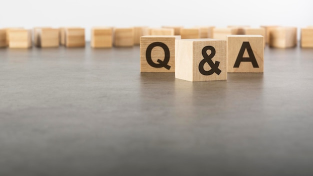 Three wooden blocks with letters Q and A with focus to the single cube in the foreground in a conceptual image on grey background