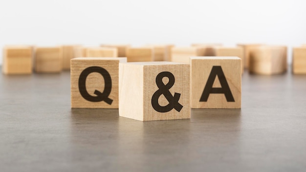 Three wooden blocks with letters Q and A with focus to the single cube in the foreground in a conceptual image on grey background