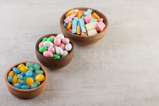 Three wooden bowls of chewing gums and candies stone table .