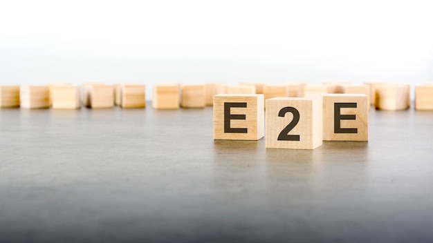 灰色のテーブルの明るい表面に E2E の文字が付いた 3 つの木製の立方体