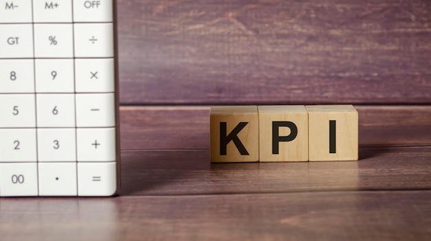 Three wooden cubes with letters KPI on the wooden table and calculator