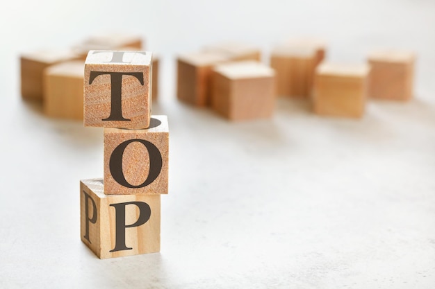 Three wooden cubes with word TOP, on white table, more in background, space for text in right down corner