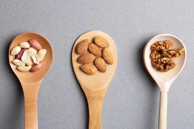 Three wooden spoon with almonds, peanuts and walnuts