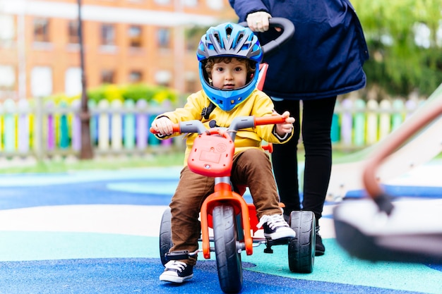 Three year old boy riding a tricycle with a helmet in a park