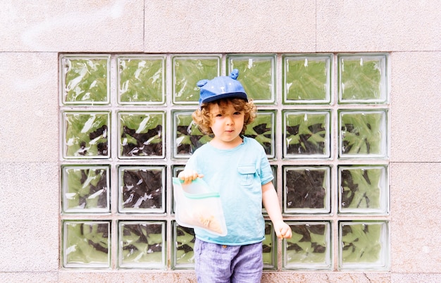 Трехлетний мальчик в синей кепке перекусывает на улице