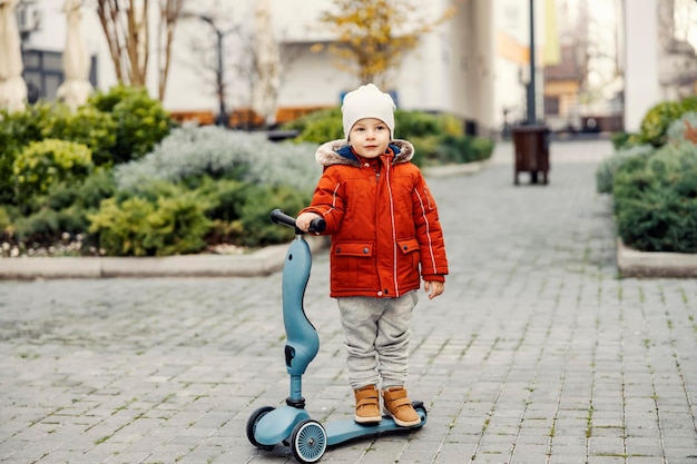 Трехлетний мальчик со скутером в парке в холодную погоду