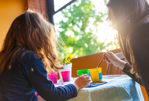 Three year old girl coloring with her mother with watercolors.