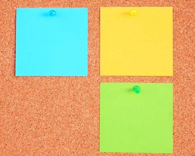 Three yellow Green and blue notes pinned on a cork bulletin board background