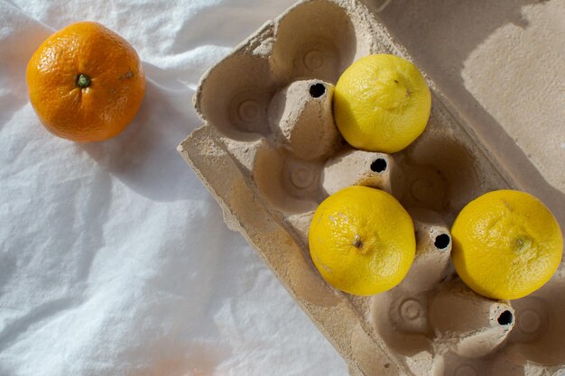 Three yellow lemons in an egg carton and one orange tangerine on a white background