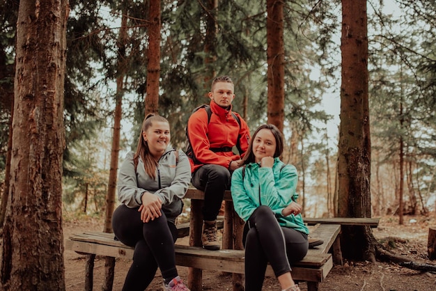 Photo three young adult friends taking a break sitting on wood desk in forest