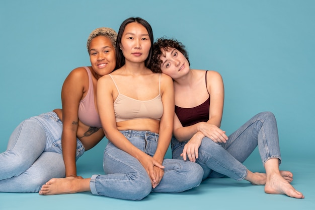 Foto tre giovani donne affettuose e amichevoli in canottiera e jeans blu sedute l'una vicino all'altra