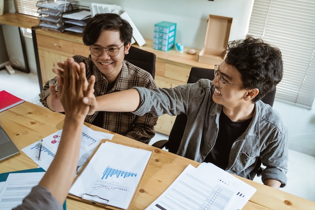 Tre giovani imprenditori asiatici lavorano insieme in accordo alla pianificazione con gesto unitario