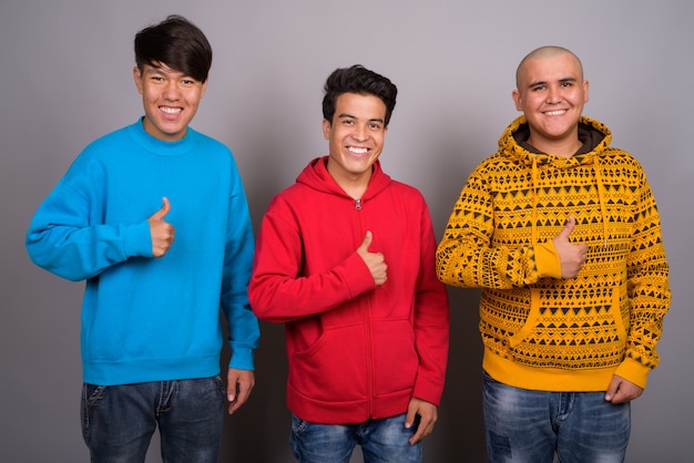 three young Asian men wearing warm clothing against gray wall